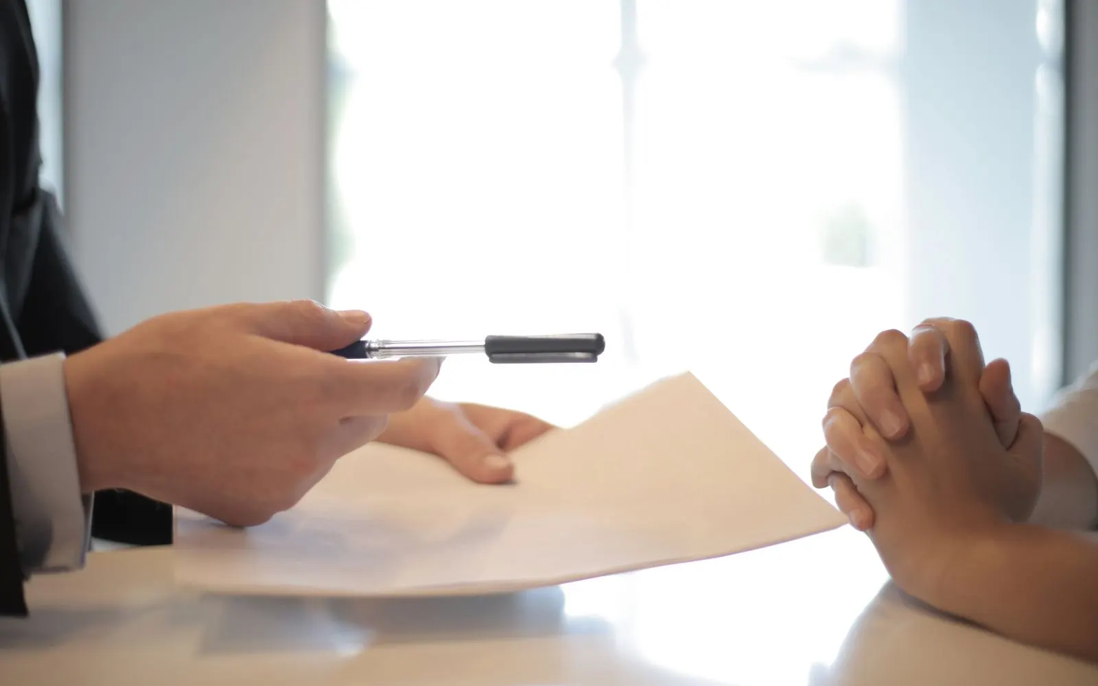 Two people at a table passing a printed document across it.