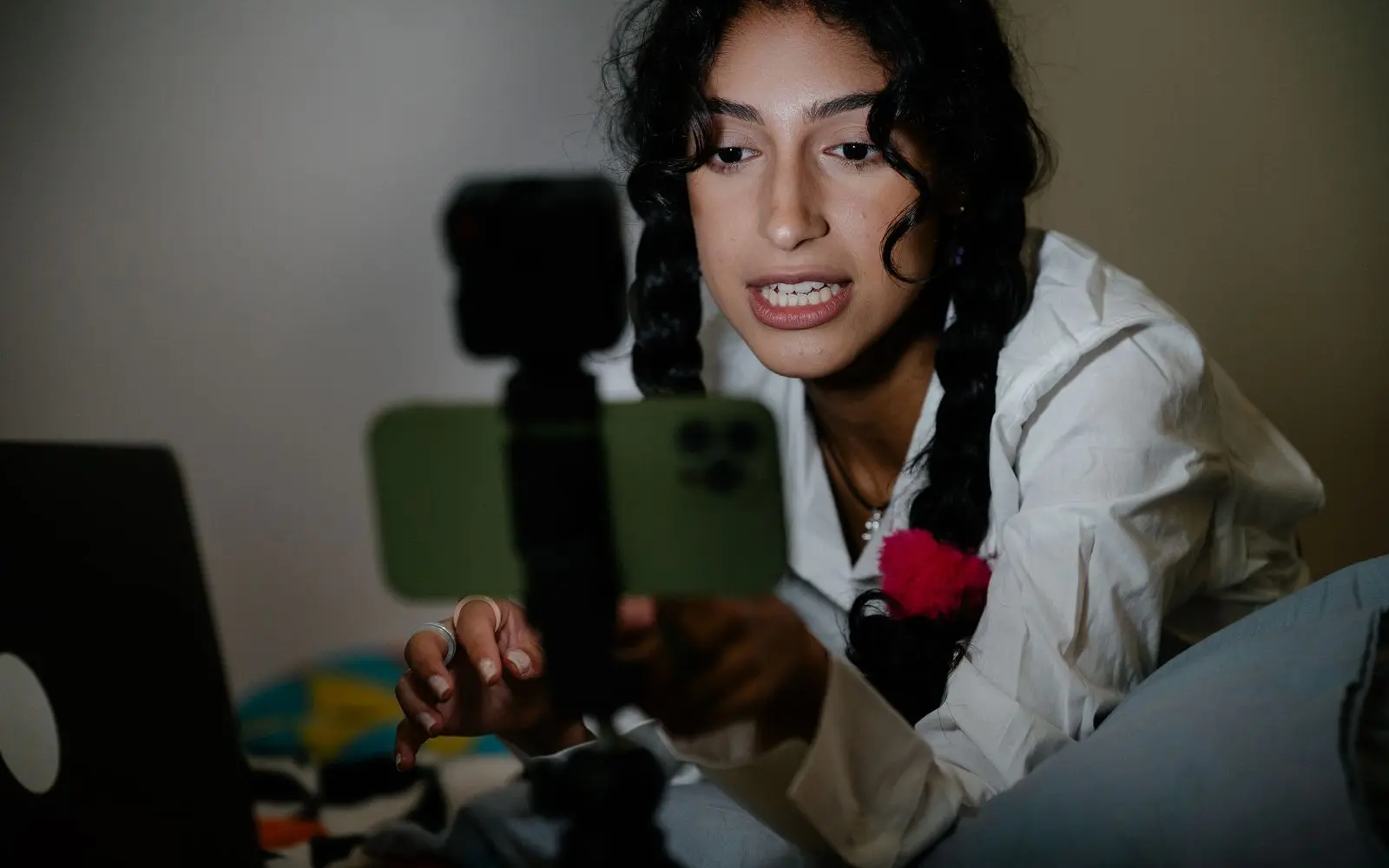 A creator talking to a phone on a small rig, with a laptop beside her.