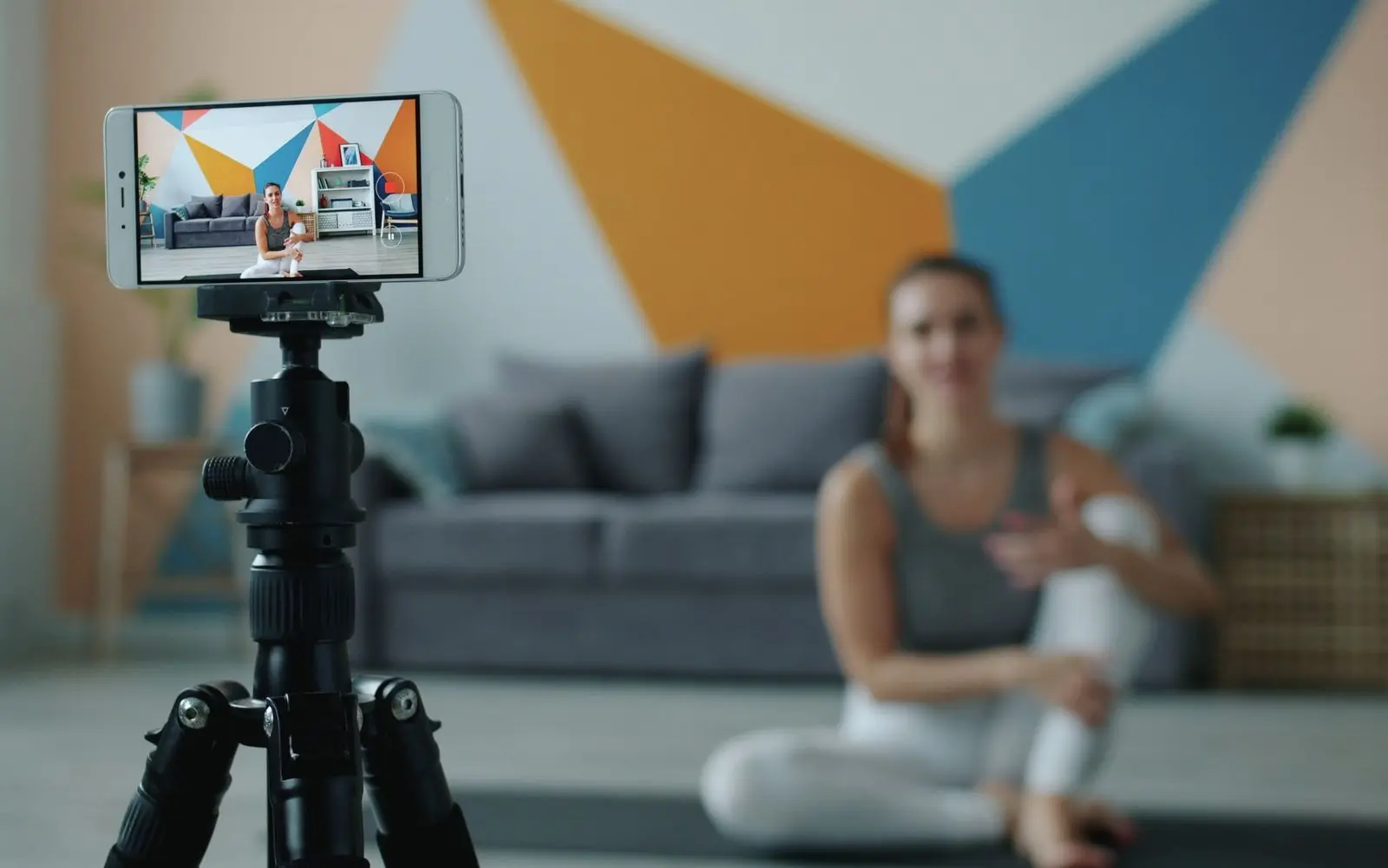 A phone on a tripod filming a creator sitting on the floor of a bright living room.