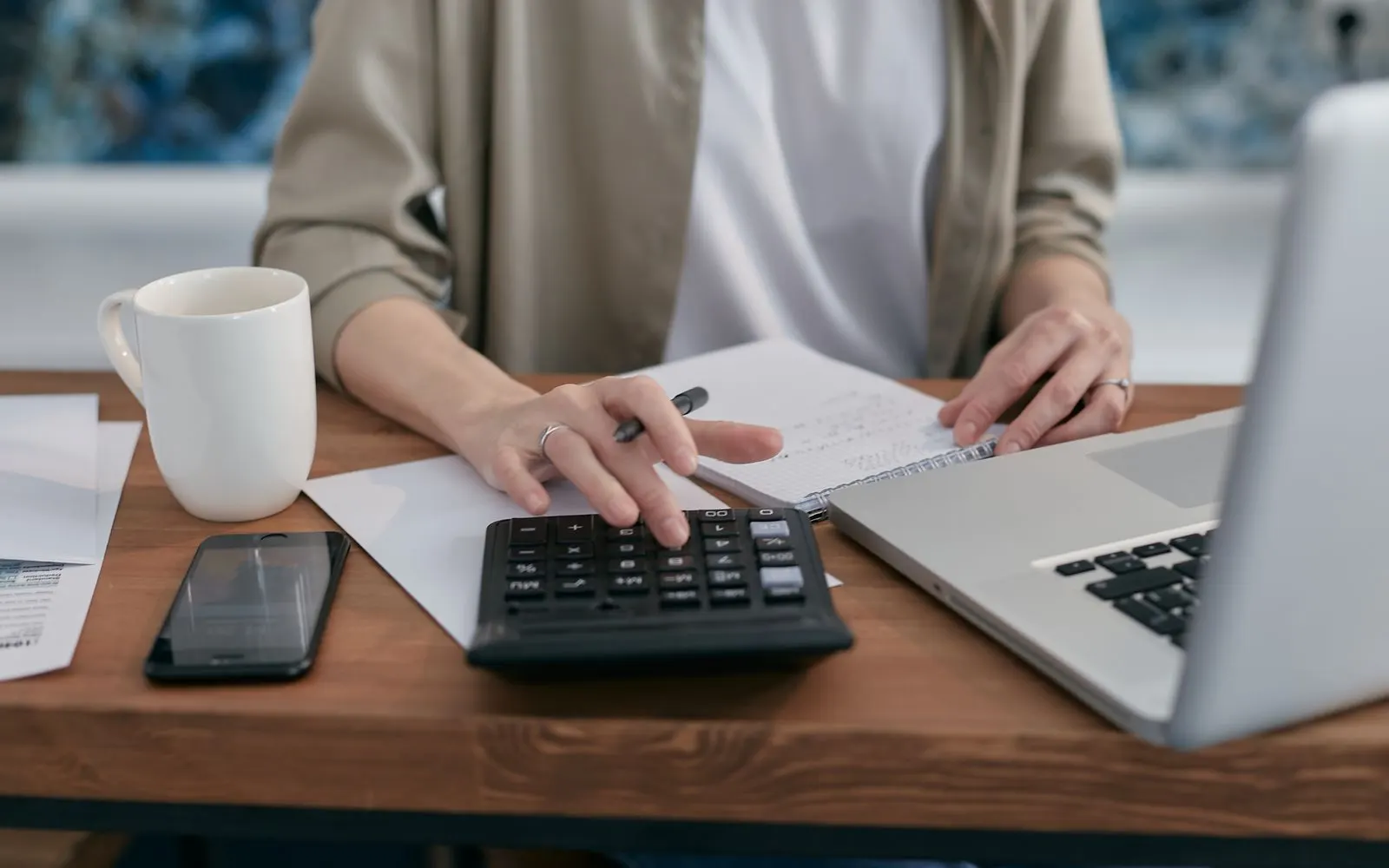 A person at a desk working through figures on a calculator beside a laptop and a notepad.