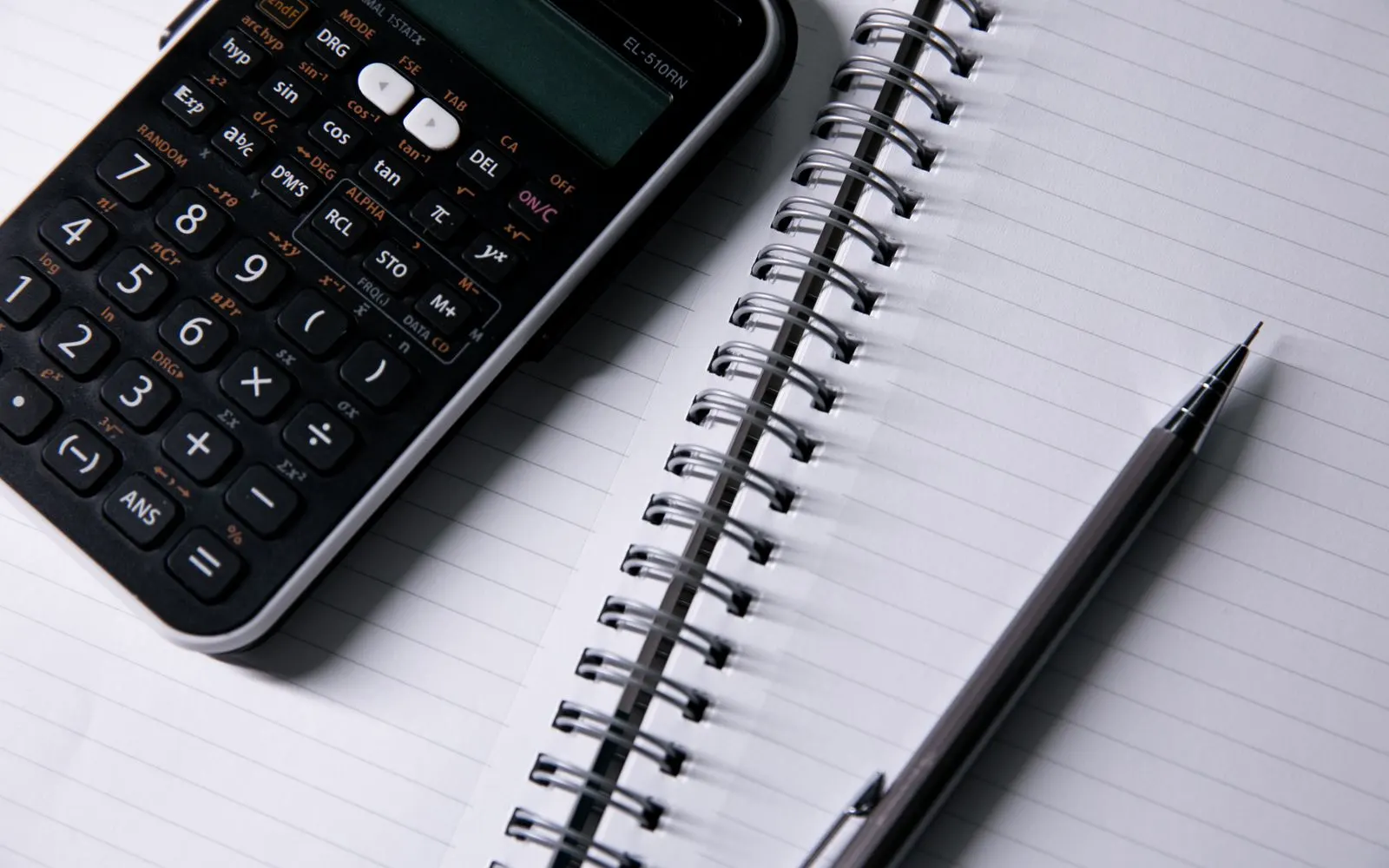 A calculator and a pen resting on an open spiral notebook.